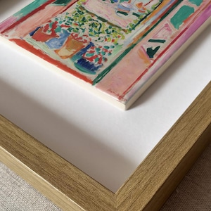 May include: A framed print of a painting featuring a colorful interior scene with potted plants, rendered in shades of pink, green, red, and blue. The artwork is set within a gold-toned frame and includes the signature Henri Matisse in the corner.