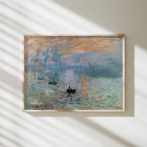May include: A framed print of Claude Monet's Impression, Sunrise, featuring a harbour scene with small boats on water, a bright orange sun, and hazy blue and grey tones. The painting includes the artist's signature and the year 72 in the corner.