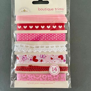 Op de afbeelding: Een pakket met roze en rode boutique-bies met verschillende patronen, waaronder harten, stippen en kant. Het pakket bevat 14 voet bies en staat er "verfris je verbeelding" op.