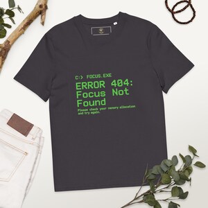 May include: Charcoal grey t-shirt featuring the text "C:> FOCUS.EXE ERROR 404: Focus Not Found" in green. The text includes the message "Please check your memory allocation and try again."
