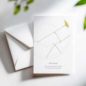 May include: A white greeting card and envelope set. The card features a minimalist design with gold lines resembling kintsugi, the Japanese art of repairing broken pottery. The text reads "Kintsugi" and a related quote.