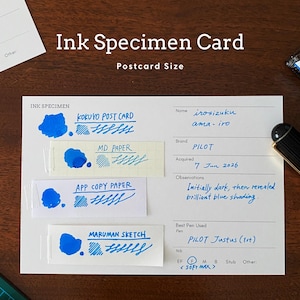 May include: A white ink specimen card with printed fields for name, brand, date, and observations. Four paper strips are attached, each showing blue ink swatches and handwritten text. The card includes the text Ink Specimen and Postcard Size.