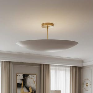 May include: A contemporary living room featuring a dark green sofa, beige armchairs, and a large rug. A marble-topped coffee table is in front of the sofa. A large, round, white ceiling light hangs above the seating area.