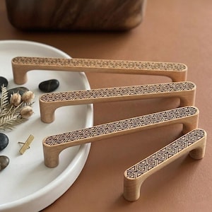 May include: Four wooden cabinet pulls with a geometric design etched into the top. The pulls are light brown and have a curved handle. The geometric design is a series of triangles. The pulls are arranged on a brown surface.