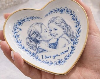 May include: Heart-shaped trinket dish with a blue and white floral design and a gold rim. The dish features a portrait of a mother and child with the text "I love you, mom!" A decorative piece for jewelry or small items.