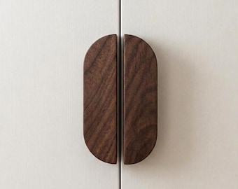 May include: Two semi-oval dark brown wooden cabinet handles mounted vertically on a light off-white cabinet door. The handles feature a visible wood grain pattern and are positioned side-by-side to form a complete oval shape when closed.