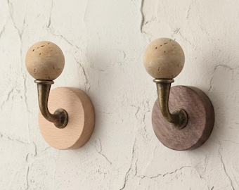 May include: Two wooden wall hooks. One hook has a light wood base and the other has a dark wood base. Each hook has a brass-colored curved arm and a spherical, textured, beige-colored top.