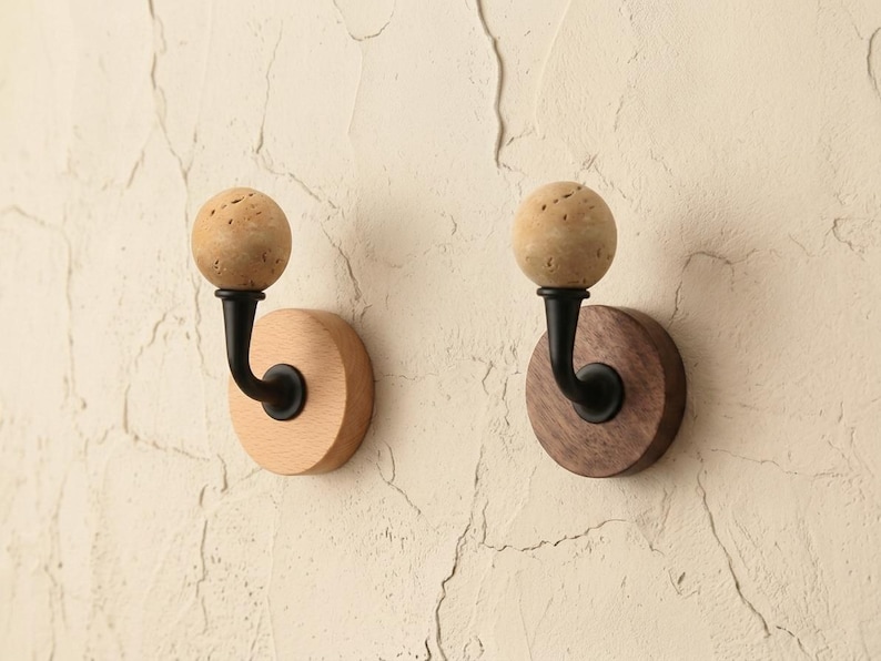May include: Two wooden wall hooks. One hook has a light wood base and the other has a dark wood base. Each hook has a black metal curved arm and a spherical, textured, light brown top.