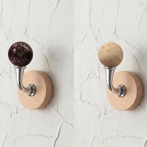 May include: Two decorative wall hooks. One features a dark maroon marble sphere, the other a light tan cork sphere. Both have a curved silver metal hook attached to a round, light-colored wooden base.
