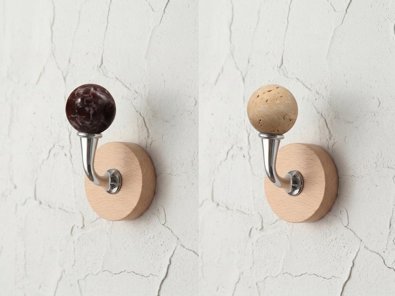May include: Two decorative wall hooks. One features a dark maroon marble sphere, the other a light tan cork sphere. Both have a curved silver metal hook attached to a round, light-colored wooden base.