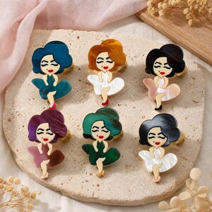 May include: Six decorative cabinet knobs shaped like stylized figures with hair in various colors including blue, brown, black, purple, and green. Each figure wears a dress that flares out at the bottom, with painted facial features and red lips.