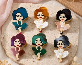 May include: Six decorative cabinet knobs shaped like stylized figures with hair in various colors including blue, brown, black, purple, and green. Each figure wears a dress that flares out at the bottom, with painted facial features and red lips.