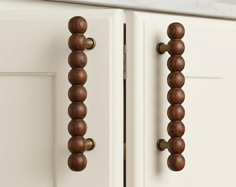 May include: Two vertical cabinet handles made of dark brown wood, each featuring a series of eight spherical beads stacked in a column. The wooden beads are attached to the cream-colored cabinet doors by two small, cylindrical brass-toned metal mounts.