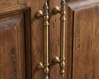 May include: Two vertical brass cabinet handles with a cylindrical shaft and decorative finials at the top and bottom, mounted on a pair of dark brown wooden cabinet doors featuring a visible wood grain and a distressed, textured surface finish.