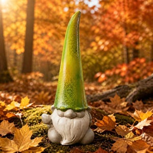 Op de afbeelding: Een tuinkabouterfiguur met een hoge, puntige muts met een glanzende, groen-gele kleurverloopafwerking. De kabouter heeft een gladde, lichtgrijze basis, een ronde neus en een getextureerde baard die het onderste deel van het figuur bedekt.