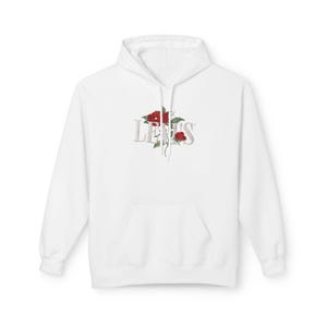 May include: White hoodie with a front pocket and a hood. The hoodie features the word "LEERS" in a stylized font, with red roses and green leaves incorporated into the design. The overall aesthetic is clean and modern.
