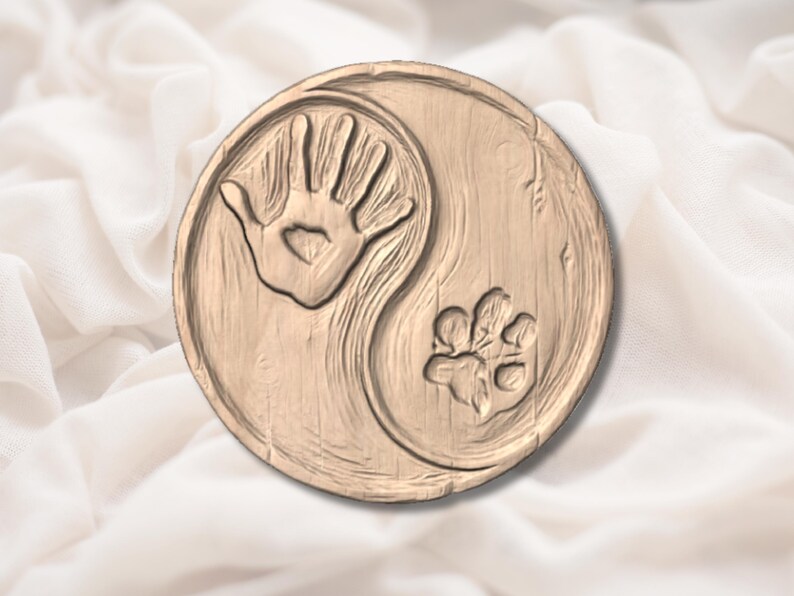 Peut inclure: Plaque ronde en bois avec un motif Yin Yang. Un c&ocirc;t&eacute; pr&eacute;sente une empreinte de main avec un c&oelig;ur d&eacute;coup&eacute;, l'autre une empreinte de patte. La plaque est de couleur marron clair et repose sur un fond blanc textur&eacute;.