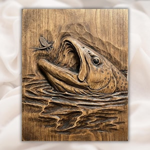 May include: A wooden relief carving depicts a fish leaping from water to catch a mayfly. The artwork is rendered in shades of brown, with detailed textures of water and fish scales. The fish's mouth is open, capturing the insect.