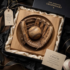 May include: A wooden carving of a baseball glove and ball set inside a square wooden frame, presented in a black gift box with cream satin lining. Includes a tag reading FOR A LEGEND ON AND OFF THE FIELD and a card stating THANK YOU COACH.