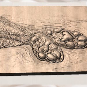 May include: A detailed wooden carving of a dog's paw and leg. The carving showcases the texture of the fur and the pads of the paw. The artwork is displayed on a rectangular wooden surface, with the grain of the wood visible.