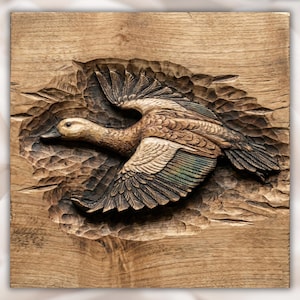 May include: A detailed wood carving of a duck in flight. The duck is carved in a naturalistic style, with its wings spread wide. The wood has a warm, brown tone, and the carving is set against a textured background. The duck's feathers have hints of green.