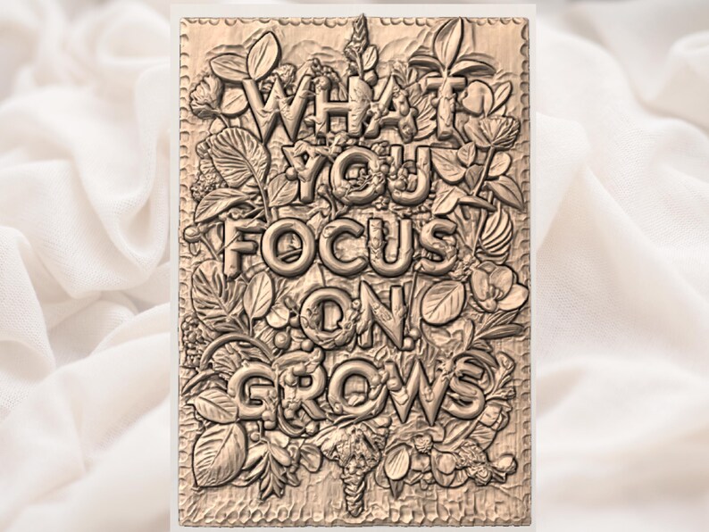Puede incluir: Placa rectangular de madera con las palabras "WHAT YOU FOCUS ON GROWS" talladas en letras en relieve. Las letras est&aacute;n rodeadas de tallas detalladas de hojas, flores y otros elementos bot&aacute;nicos. La placa tiene un tono de madera natural.