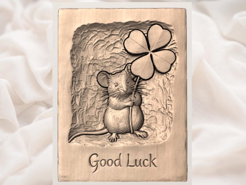 May include: A rectangular, light brown plaque with a carved image of a mouse holding a four-leaf clover. The words "Good Luck" are carved at the bottom. The background has a textured, cave-like appearance.