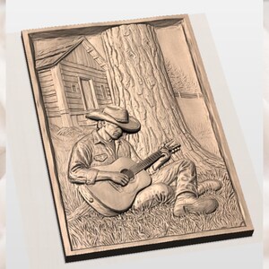 May include: A detailed relief carving shows a person playing a guitar under a tree, with a small cabin in the background. The artwork is framed and features a cowboy hat and boots. The carving is in shades of brown and tan.