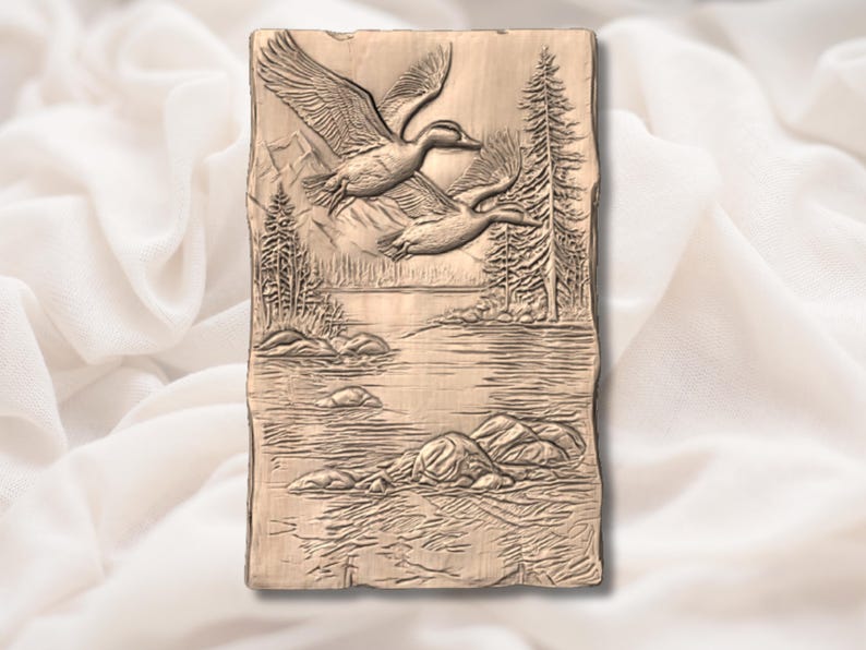 May include: A rectangular, bronze-coloured relief carving showing two ducks in flight over a lake and forest scene. The ducks are in mid-flight with outstretched wings. The background includes trees, mountains, and water.