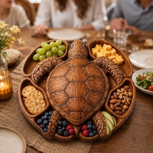 May include: A brown wooden serving tray shaped like a sea turtle with a textured shell and flippers. The tray features multiple carved compartments filled with green grapes, cubed yellow cheese, round crackers, mixed nuts, blueberries, raspberries, and apple slices.