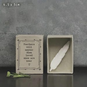 May include: A small, open matchbox containing a white feather, beside a closed matchbox with the text "Feathers will appear when loved ones are near." The matchboxes measure 4.5 x 3 cm.