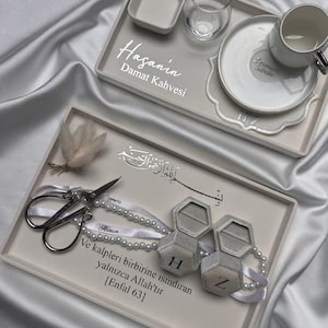 Peut inclure: Deux plateaux rectangulaires blanc cassé avec du texte personnalisé et des objets décoratifs. Un plateau contient une tasse à café, une soucoupe et un verre. L'autre plateau contient des ciseaux argentés, deux boîtes à bagues hexagonales H et Z.
