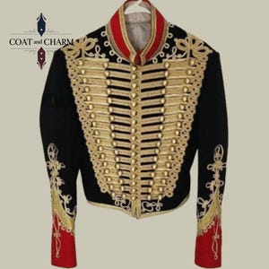 May include: Black military-style jacket with gold embellishments and buttons. The jacket features a red collar and cuffs, and intricate gold embroidery on the sleeves and front. The jacket is hanging on a white hanger.