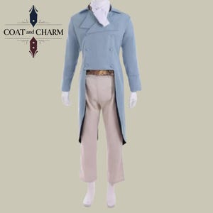 May include: A light blue double-breasted coat with a long tail, paired with beige pants. The outfit includes a white ascot and a decorative belt. The logo "COAT and CHARM" is visible in the upper left corner.
