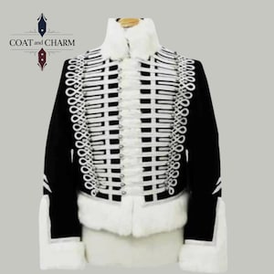 May include: A black and white military-style jacket with intricate white detailing and a high collar. The jacket features rows of white trim and decorative elements, with a faux fur collar and cuffs. The brand name "COAT and CHARM" is visible on the left side.