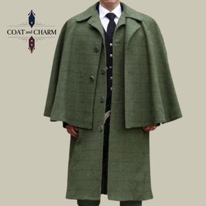 May include: A green tweed coat with a matching cape. The coat has a classic design with a button-up front and a collared neckline. The cape is attached to the coat and drapes over the shoulders. The coat is a medium length and has a subtle plaid pattern. The text "COAT and CHARM" is in the upper left corner.