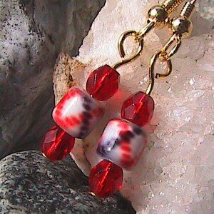 May include: Gold earrings with red and white glass beads. The beads have a white background with red and black swirls.