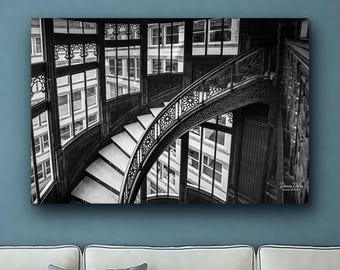 Könnte beinhalten: Ein schwarz-weiß Wandkunstdruck, der eine geschwungene Treppe mit kunstvollen Metallgeländern und großen Fenstern zeigt. Die Komposition fängt architektonische Details und Lichtreflexionen ein. Die Signatur Dennis Dlee Good Photos ist sichtbar.