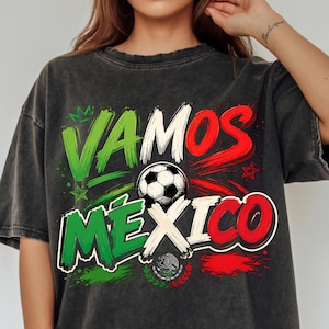 May include: A charcoal grey oversized t-shirt featuring the text VAMOS MEXICO in green, white, and red lettering. A football graphic is positioned in the centre, accompanied by a small emblem of the Mexican coat of arms below the text.
