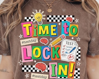 May include: Brown t-shirt with a colorful graphic that says "Time to Lock In!" The design includes a lightbulb, brain, pencil, test paper, and stars. The words are in various bright colors, with the hashtag #testday.