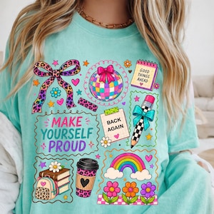 Peut inclure: Un t-shirt à manches courtes vert menthe avec un imprimé graphique coloré. Le motif comprend un nœud à motif léopard, une boule à facettes, un crayon, un arc-en-ciel, des fleurs, un café et un sac à dos, avec le texte "MAKE YOURSELF PROUD".