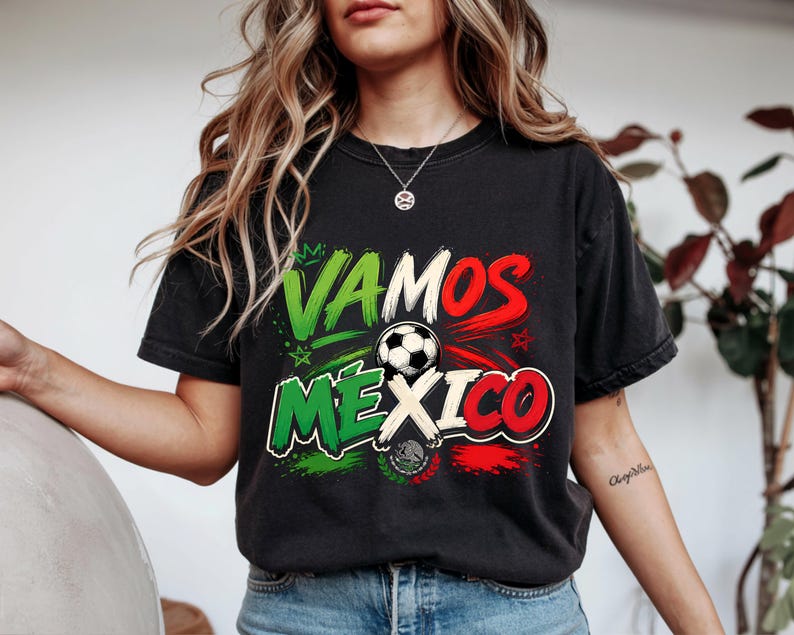 May include: A black short-sleeve t-shirt featuring a graphic print with the text VAMOS MEXICO in green, white, and red. The design includes a football, small star icons, and a central emblem resembling the Mexican coat of arms in colour.