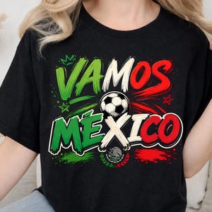May include: A black short-sleeved t-shirt featuring a graphic print with the text VAMOS MEXICO in green, white, and red brushstroke lettering. A black and white football is centred in the design, accompanied by a small crown and star icons.