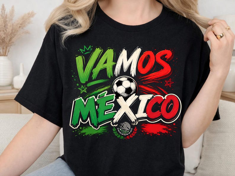 May include: A black short-sleeved t-shirt featuring a graphic print with the text VAMOS MEXICO in green, white, and red brushstroke lettering. A black and white football is centred in the design, accompanied by a small crown and star icons.