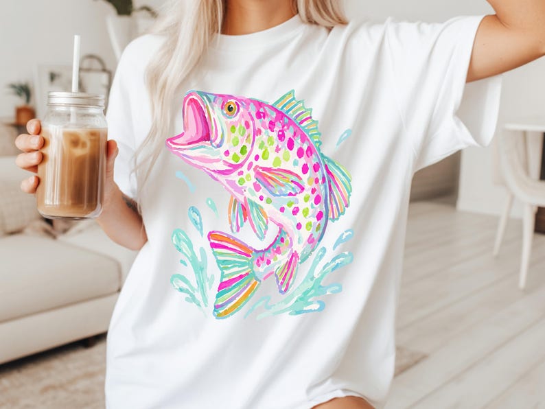 May include: White t-shirt featuring a colorful watercolor illustration of a jumping fish. The fish is depicted in shades of pink, green, blue, and yellow, with water splashes around it. The shirt is a casual, everyday wear item.