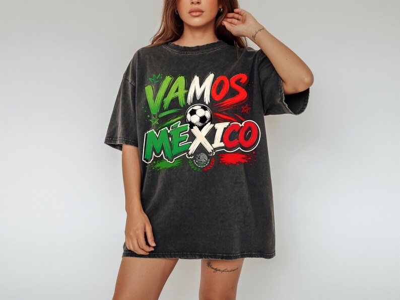 May include: A charcoal grey oversized t-shirt featuring the text VAMOS MEXICO in green, white, and red lettering. A football graphic is positioned in the centre, accompanied by a small emblem of the Mexican coat of arms below the text.