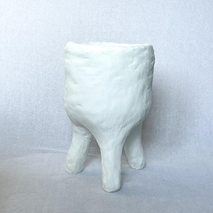 Może przedstawiać: Biała, ręcznie robiona ceramiczna donica o teksturowanej powierzchni. Donica ma cylindryczny korpus wsparty na trzech solidnych nogach, tworząc unikalną i nowoczesną estetykę. Idealna do małych roślin.