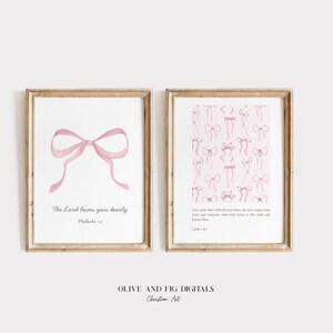 Pode incluir: Duas impressões emolduradas com desenhos de laços rosa em aquarela. Uma impressão apresenta um único laço com o texto "The Lord loves you dearly". A outra impressão tem um padrão de laços com texto. Ambas em molduras de madeira clara.