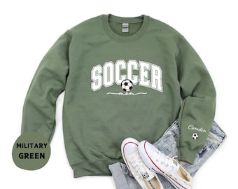 May include: Military green sweatshirt with the word "SOCCER" in white block letters and a soccer ball graphic. The word "mom" is written below the soccer ball. The sleeve has the name "Camden" and a soccer ball graphic.