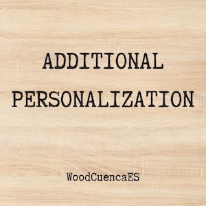以下が含まれることがあります： 明るい茶色の木材の表面に、太字の黒いフォントで「ADDITIONAL PERSONALIZATION」という文字が書かれています。「WoodCuencaES」という文字が下部に小さく表示されています。
